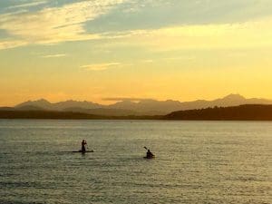 Photo of two people on paddle boards at sunset 